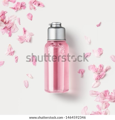 cosmetics packaging design concept or mock-up with blank transparent bottle with pink liquid soap or shower gel on a white surface surrounded by delicate cherry flower petals, top view / flat lay