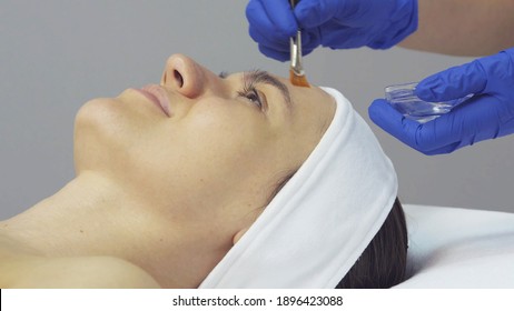 The cosmetologist applies acid to the client's face in the beauty salon