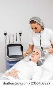 A cosmetologist applies anesthetic cream to a young woman's face before a facial cosmetic procedure. Anesthetic cream. Preparation for healing, tightening, skin rejuvenation in beauty salons. - Shutterstock ID 2365408229