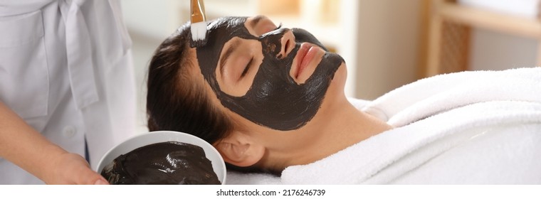 Cosmetologist Applying Black Mask Onto Woman's Face In Spa Salon. Banner Design