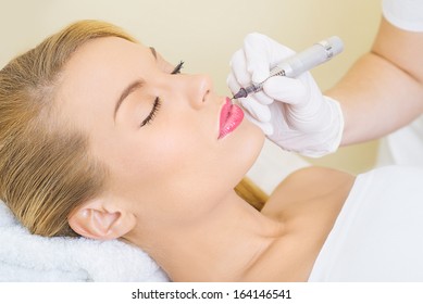 Cosmetologist applying permanent make up on lips