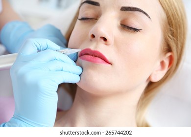 Cosmetologist applying permanent make up on lips