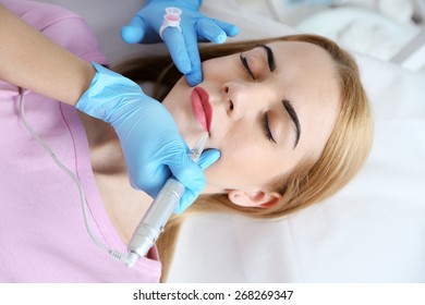 Cosmetologist applying permanent make up on lips