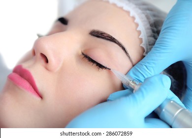 Cosmetologist applying permanent make up on eyes, close-up