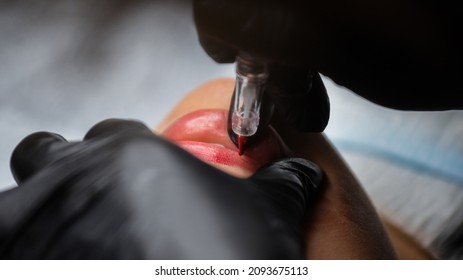 Cosmetologist in black gloves making permanent makeup on woman's lips with tattoo pen machine. Microblading process