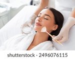 Cosmetologist cleaning face of a beautiful European woman with special gel before applying mask, peeling or scrub. Facial skin care procedures in beauty salon