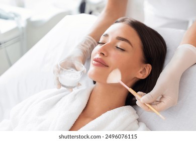 Cosmetologist cleaning face of a beautiful European woman with special gel before applying mask, peeling or scrub. Facial skin care procedures in beauty salon