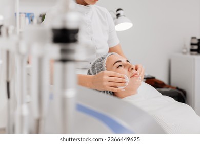 Cosmetologist cleansing patient's face with cotton pads. Woman receiving ultrasound facial peeling and cleansing. Cosmetology and face skin care. Facial treatment - Shutterstock ID 2366449625