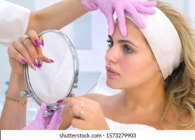 Cosmetologist is consulting woman client who looking at mirror in beauty clinic. Beauty industry concept. Beautician preparing patient to skin care procedure in spa salon, portrait of woman.
