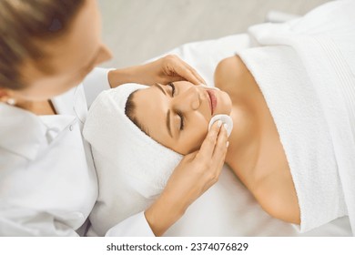 Cosmetologist doing skincare treatment for a young pretty woman in spa salon. Portrait of a female client lying in beauty clinic having a face massage and receiving beauty procedure from beautician.