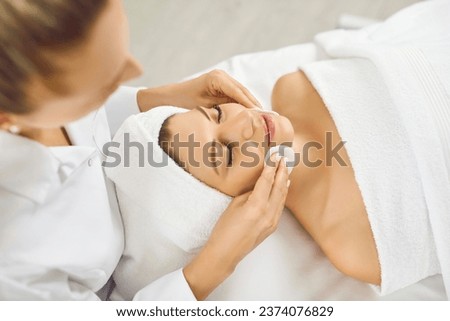 Cosmetologist doing skincare treatment for a young pretty woman in spa salon. Portrait of a female client lying in beauty clinic having a face massage and receiving beauty procedure from beautician.