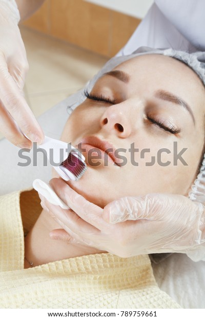 Cosmetologist hands at chin micro needling\
procedure. Vertical closeup\
shot
