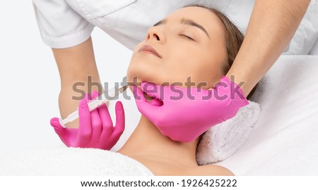 Cosmetologist makes lipolytic injections to burn fat on the chin, cheeks and neck of a woman against double chin. Female aesthetic cosmetology in a beauty salon.Cosmetology concept.