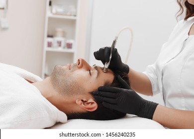 The cosmetologist makes the procedure Microdermabrasion of the facial skin of a man in a beauty salon.Cosmetology and professional skin care.