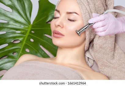 The cosmetologist makes the procedure Microdermabrasion on the face and collarbone of a beautiful woman in a beauty salon.Cosmetology and professional skin care.
