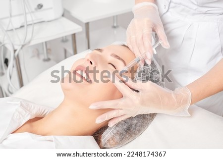 Cosmetologist makes rejuvenation injection in woman face skin, anti aging revitalization cosmetic procedure in beauty spa salon. Beautician hands in gloves makes facial acid injection treatment