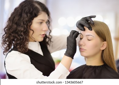 Cosmetologist making eyebrows design. Attractive woman getting facial care at beauty salon. Perfect architecture eyebrows.