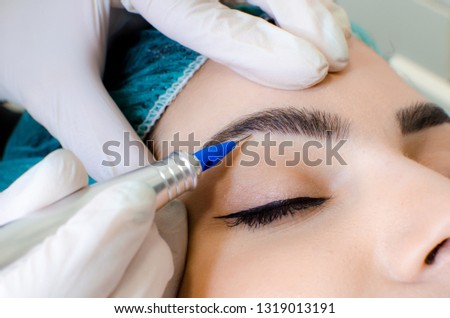 Cosmetologist making permanent make up on eyebrows, tattoo procedure on young woman in beauty salon, extreme close up