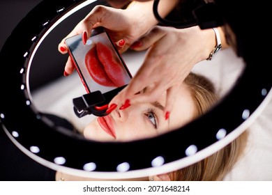 Cosmetologist Making Photo Of Work On Mobile Phone Red Permanent Make Up Tattoo On Young Woman Lips.