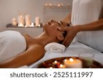 Cosmetologist masseur making relaxing head massage for young lady at modern luxury spa in romantic serene atmosphere with candles