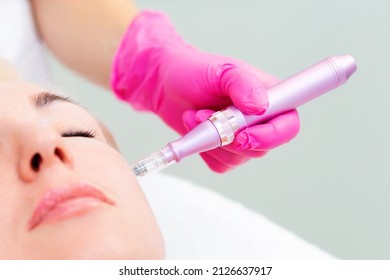 A cosmetologist in medical pink gloves does mesotherapy on the cheek of a beautiful woman. Close up of face. The concept of aesthetic medicine and hardware cosmetology.