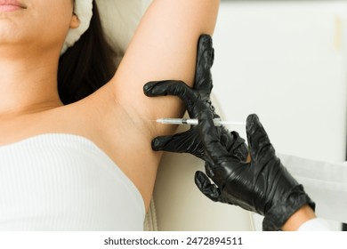 Cosmetologist performing botulinum toxin injection in patient's underarm for hyperhidrosis in clinical setting - close-up shot