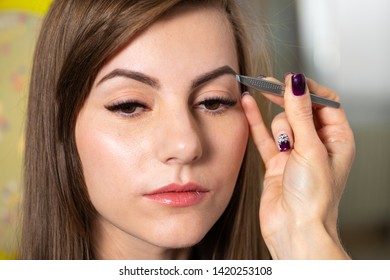 Cosmetologist plucks client eyebrows by tweezers