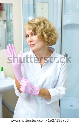 Cosmetologist prepares for the apparatus procedure of ultrasound cleaning of the facial skin. Putting on pink latex gloves. Beauty facial treatment. Lifting effect.