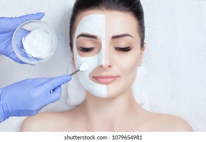 The Cosmetologist For The Procedure Of Cleansing And Moisturizing The Skin, Applying A Mask With Stick To The Face Of A Woman In Beauty Salon. Cosmetology And Professional Skin Care.