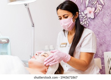 Cosmetologist at protective mask and medical gloves massages client's face. Concept of professional cosmetology and new normal.