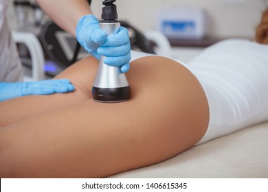 Cosmetologist reducing cellulite on the hips of a female patient, using ultrasound cavitation machine. Cropped shot of a woman getting slimming procedure at beauty salon