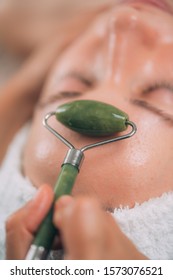 Cosmetologist using jade stone roller for Guasha face drainage massage