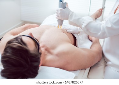 Cosmetologist using modern laser device to remove chest hair of man