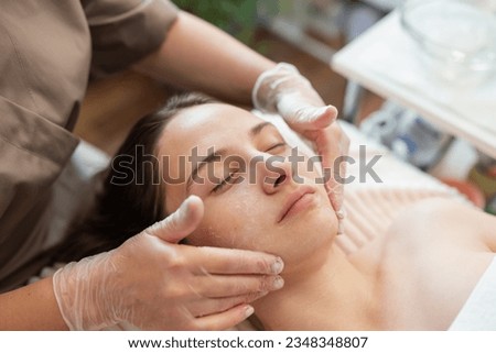 Cosmetologist washing and cleaning client face before procedure of ultrasound face cleaning. Preparations before ultrasonic face cleaning procedure on female face