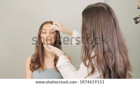 Cosmetologist wiping eyebrows using cotton pads. Beautician rubs client's face with a cotton pad. Beautician in gloves is doing permanent makeup to girl. Eyebrow correction.
