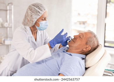 In cosmetology clinic, female doctor administers injection and skillfully performs lip augmentation procedure on senior man patient. - Powered by Shutterstock