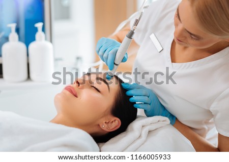 Cosmetology clinic. Professional female cosmetologist doing hydrafacial procedure while being a work
