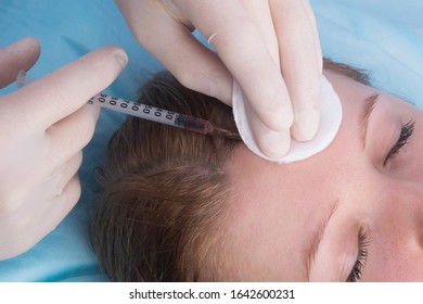 cosmetology, hands in sterile gloves, make a beauty injection to a woman with closed eyes, in the frontal part, close-up