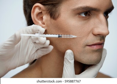 Cosmetology. Portrait Of Handsome Man With Perfect Skin Getting Beauty Treatment Indoors. Closeup Of Beautician Hands Injecting Filler Injection On Male Face. Skin Lift Procedure. High Resolution