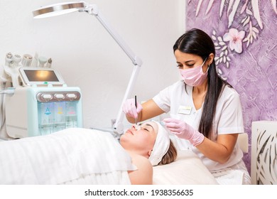 Cosmetology. Professional cosmetologist in a medical mask and rubber gloves, applies the mask to the client's face. The concept of professional care in beauty salons during the pandemic.