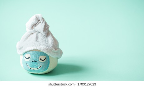 Cosmetology, Skin Care, Face Treatment, Spa And Natural Beauty Concept. Coconut With Creative Face Mask And Towel On Top . On A Blue Background. Space For Text.