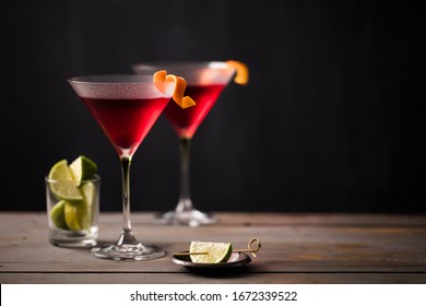 Cosmopolitan cocktails on wooden worktop.  Orange garnish. Lime wedges. Space for text