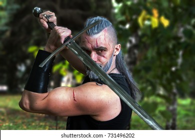 Cosplay, Dressed Like A Hero Geralt Of Rivia From The Game The Witcher, A Fantastic Warrior With A Sword In His Hands