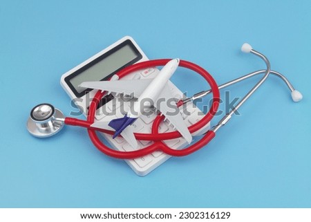Cost of ravel insurance concept. Airplane with red stethoscope on calculator on blue background.