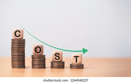 Cost wording on decreasing coins stacking with down arrow for cost reduction concept which effect to product cost , profit , inflation and economy recession concept.