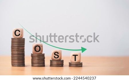 Cost wording on decreasing coins stacking with down arrow for cost reduction concept which effect to product cost , profit , inflation and economy recession concept.