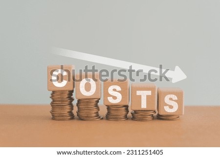 Cost wording on decreasing stack of coins stacking with white down arrow for cost reduction concept which effect to product cost , profit , inflation and economy recession concept