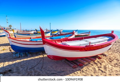 Costa Brava, Spain. Fishing boats rest on a golden sand beach overlooking the blue sea at Calella. - Powered by Shutterstock