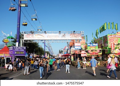 COSTA MESA, CALIFORNIA - AUG 8, 2019: Crowd Passes Under The Aerial Lift Ride And Direction Banner At The Orange County Fair.