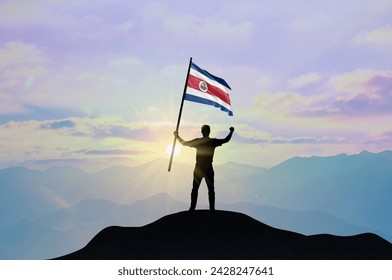 Costa Rica flag being waved by a man celebrating success at the top of a mountain against sunset or sunrise. Costa Rica flag for Independence Day. - Powered by Shutterstock